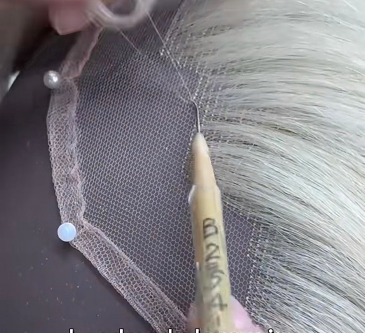 An artisan hand-tying individual hair strands into a wig cap