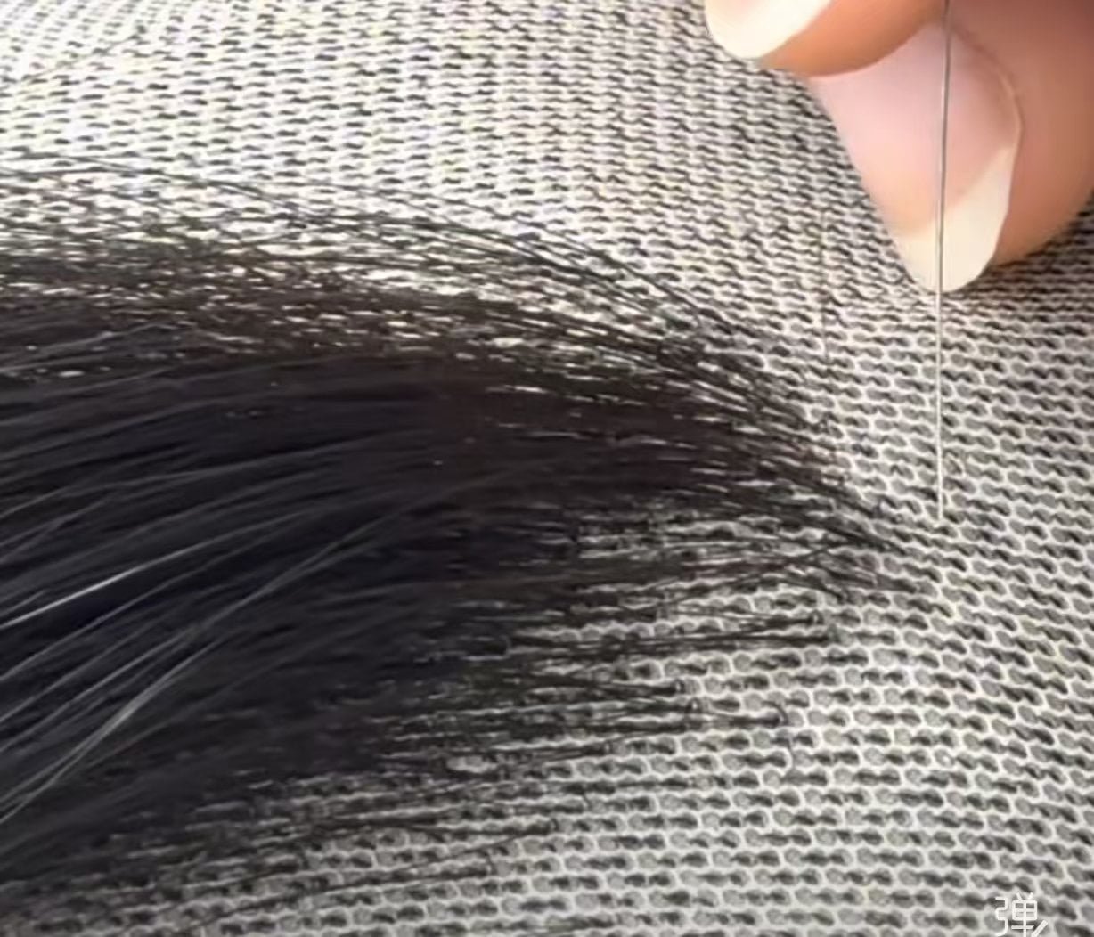 Hand-Tying a Wig A factory worker carefully hand-tying hairs onto a wig cap